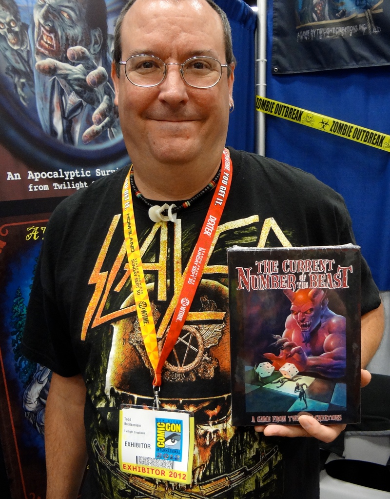 Clad in a Slayer shirt, game designer Todd Breitenstein holds up The Current Number of the Beast at Comic-Con booth