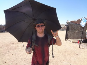 Black umbrella protects Wasteland Weekend cofounder Jared from desert heat near California City