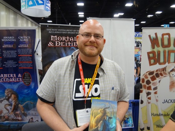 Fantasy Author J.T. Hartke holding his book A Balance Broken at his booth at Comic-Con in San Diego