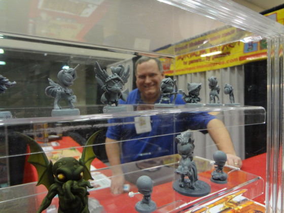 Miniature display case in foreground with tentacled Cthulu and pony while Tom Anders is in background smiling