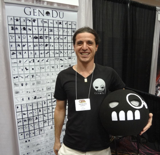 Eytan Benichay stands with Jack-in-the-box style Gen Dun head in front of poster displaying cards at GAMA Trade Show