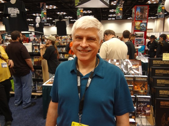 White-haired RPG Designer and Legend Kevin Siembieda smiling in crowded Gen Con Exhibitors' Hall