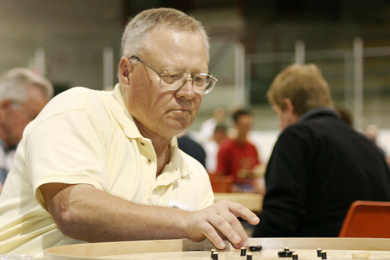 Grey-haired and with glasses Joe Fulop concentrates over a crokinole board at the 2004 World Crokinole Championship