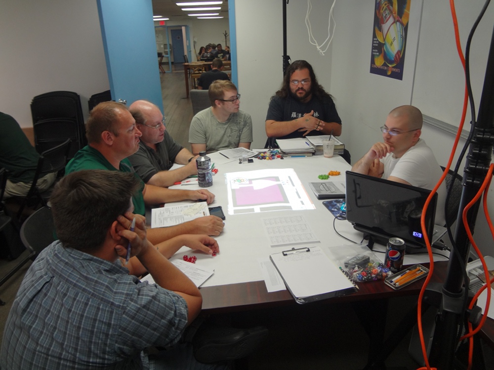 Pathfinder Society players listen attentively to GM with elaborate rig above projecting image of playing map